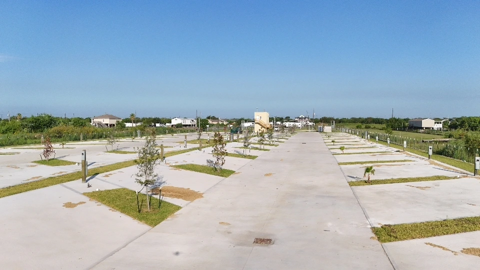 Wide concrete drive lane between landscaped RV pads under a clear Texas sky